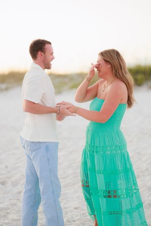 A couple in white and turquoise outfits share playful moments together on a sunny beach.