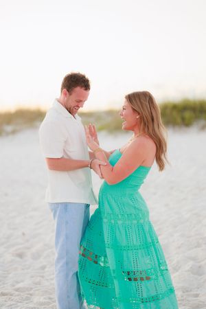 A couple shares a joyful moment together on a white sandy beach at sunset, with her wearing a bright turquoise dress.