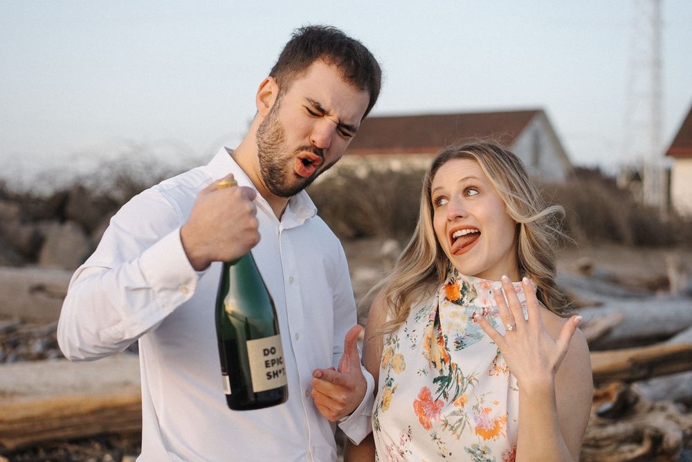 Couple in white outfits sharing romantic moments on a beach at sunset with wine glasses.