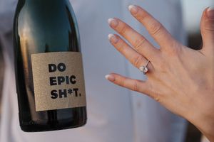 A hand wearing an engagement ring is held up against a dark background.