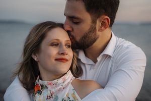 A romantic couple embraces in a tender moment against a soft outdoor backdrop during a wedding photoshoot.