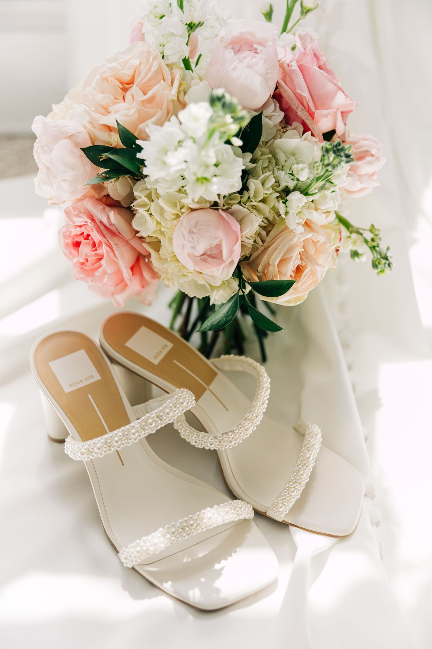 Elegant wedding shoes with lace trim displayed beside a soft pink and white floral bouquet in natural light at The Wildflower 301