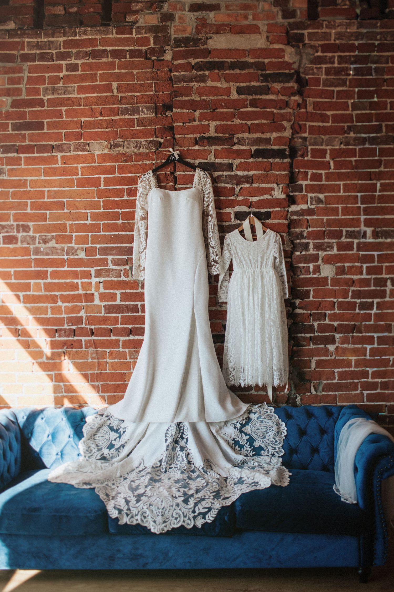 White wedding dresses displayed on a blue velvet couch against exposed brick walls.