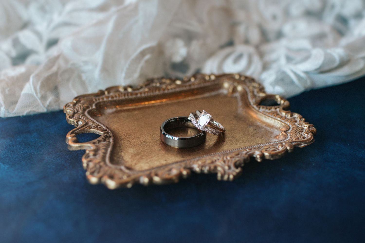 Elegant wedding rings displayed on an ornate gold vintage tray against a dark background.
