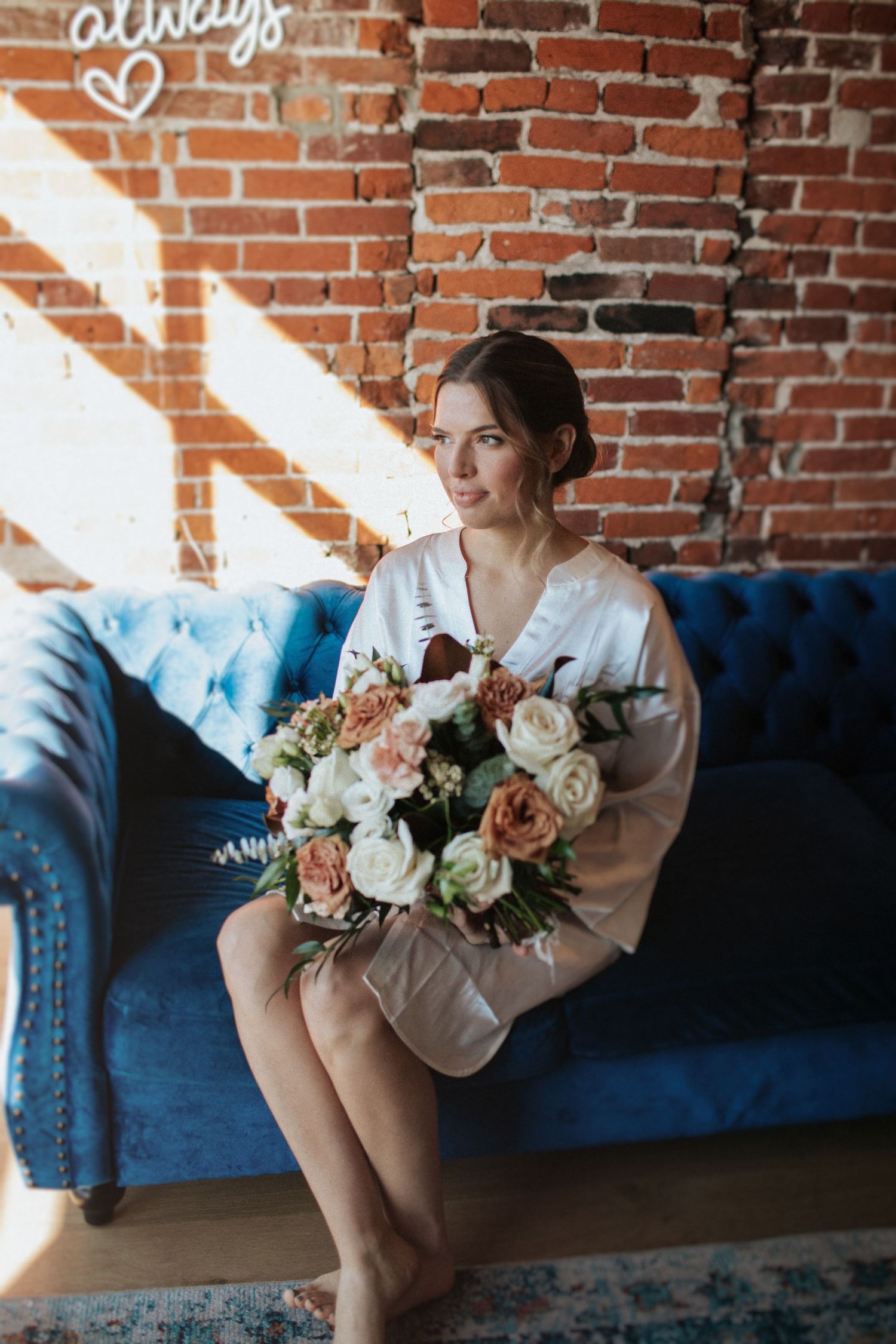 Bridal portraits on a blue velvet couch with a romantic floral bouquet against exposed brick walls.