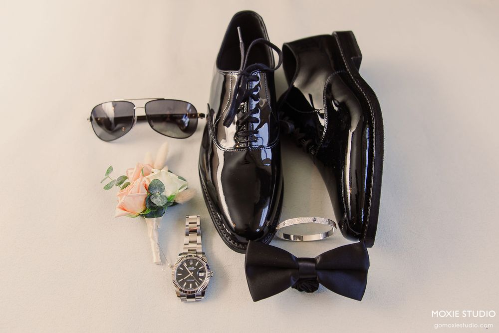 A collection of black leather shoes, sunglasses, and accessories arranged in a row on a white surface.