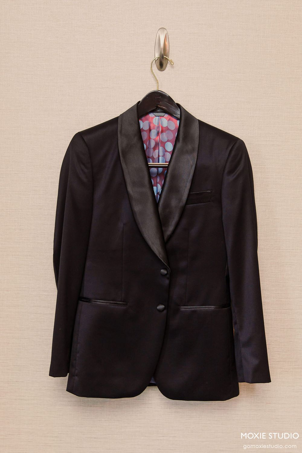 A black formal blazer jacket displayed on a hanger against a beige wall, shown from multiple angles.