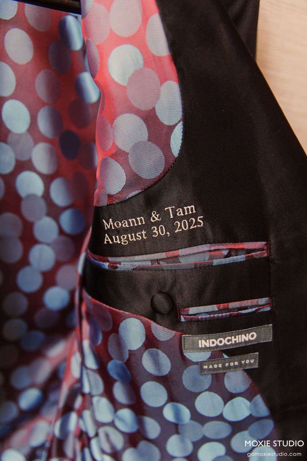Close-up view of black suit jacket lapel with custom wedding date text and polka dot pattern in background.