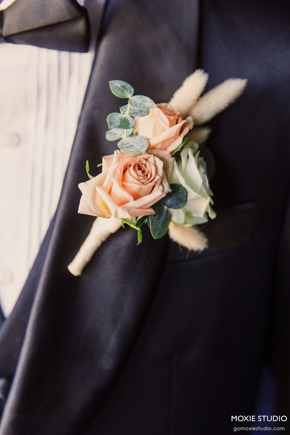 Peach rose and eucalyptus boutonniere pinned on navy blue suit jacket lapel.