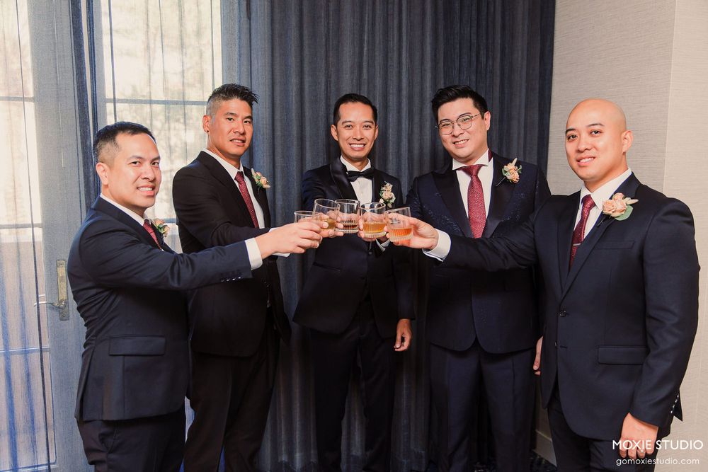 Groomsmen in matching dark suits share a celebratory toast at an indoor wedding reception.