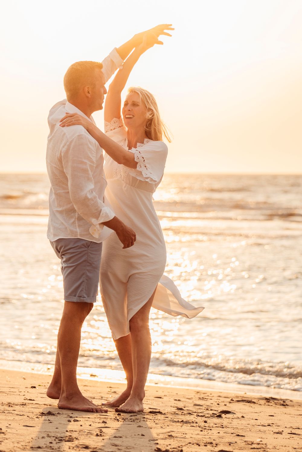 A joyful couple dancing on a sunny beach at sunset, woman raising her arm gracefully.