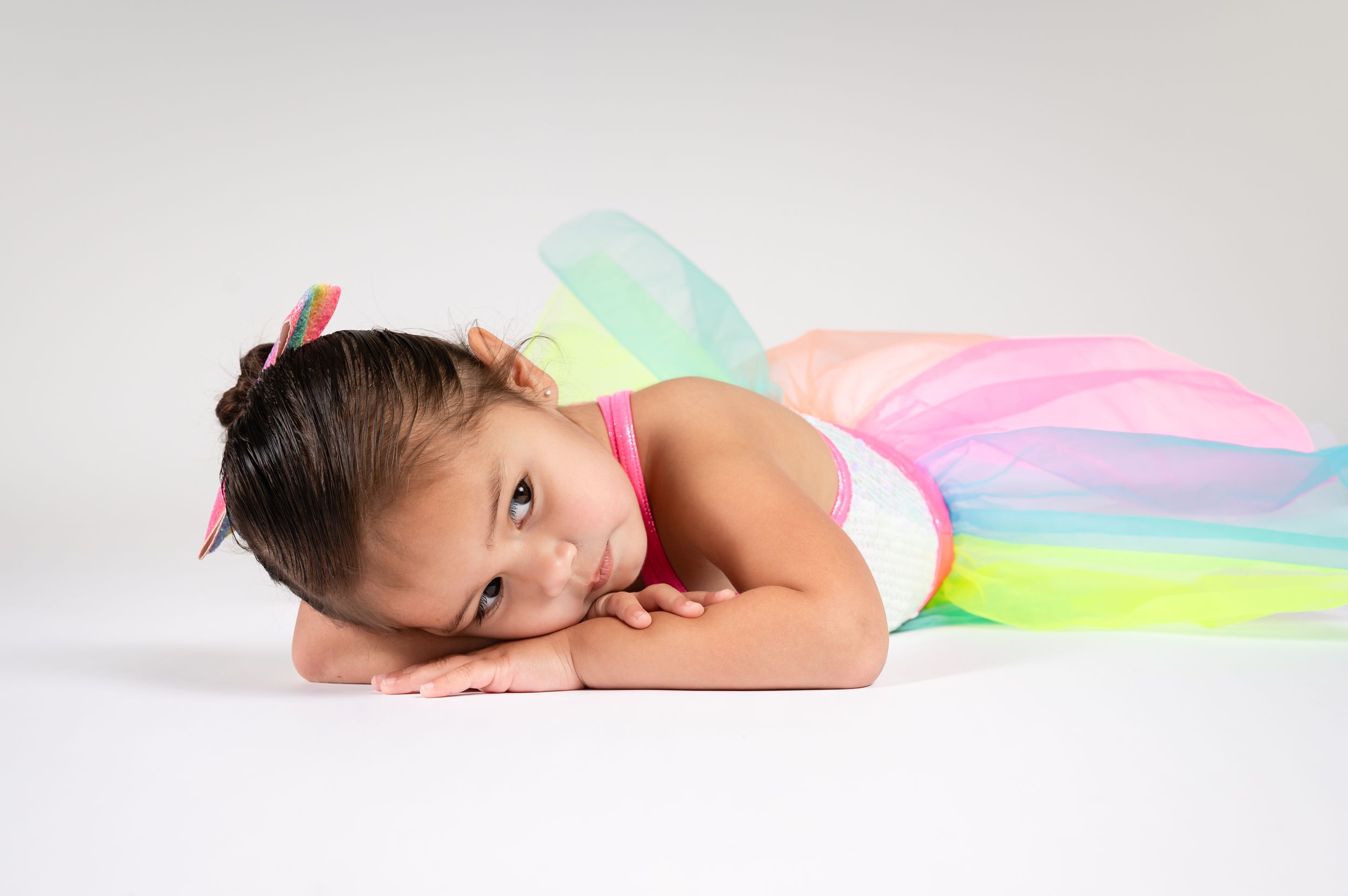 A young dancer in a colorful tutu dress lying gracefully on a white background.