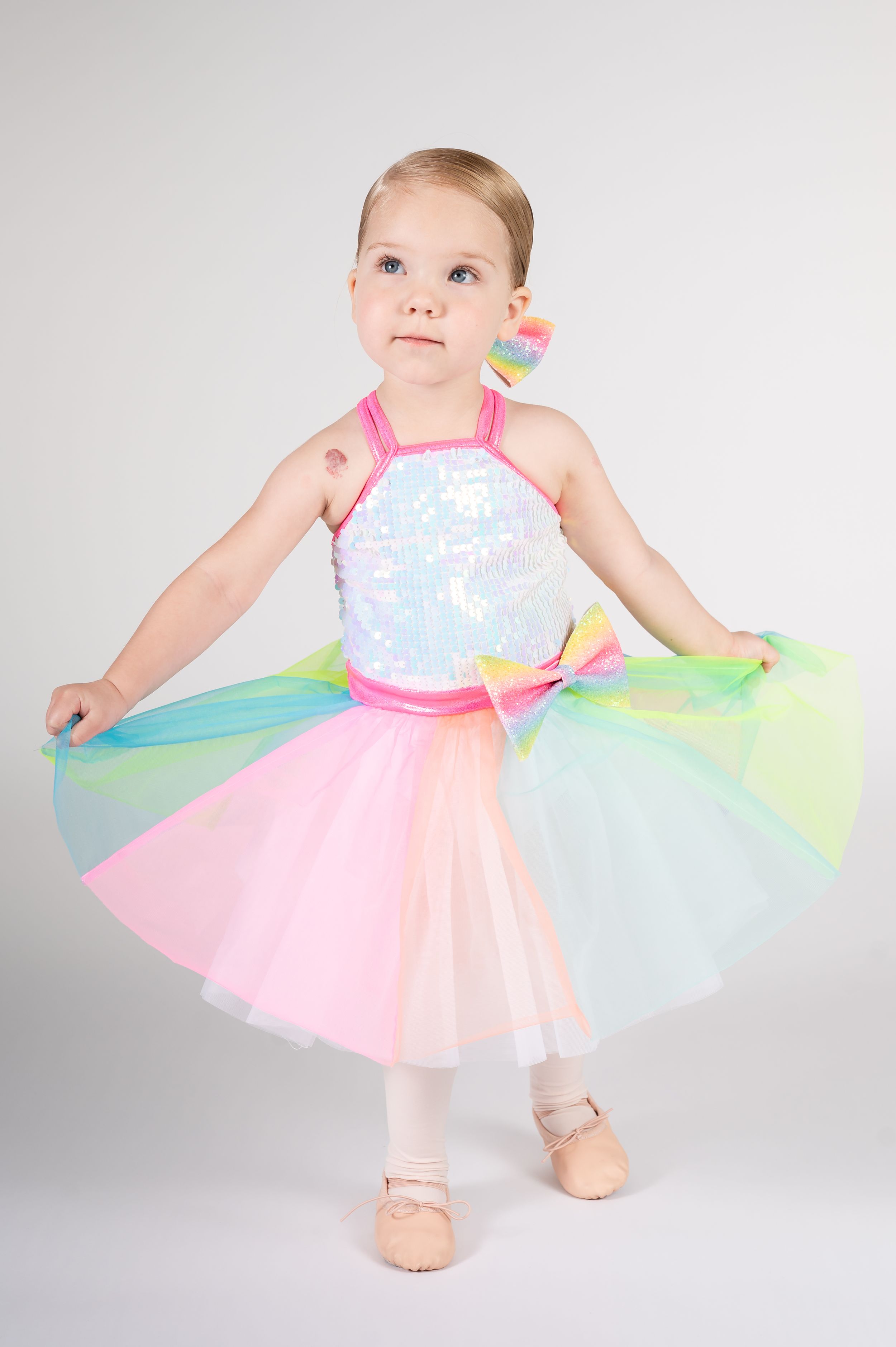 A toddler wearing a pastel tutu dress twirls and dances in a studio setting.