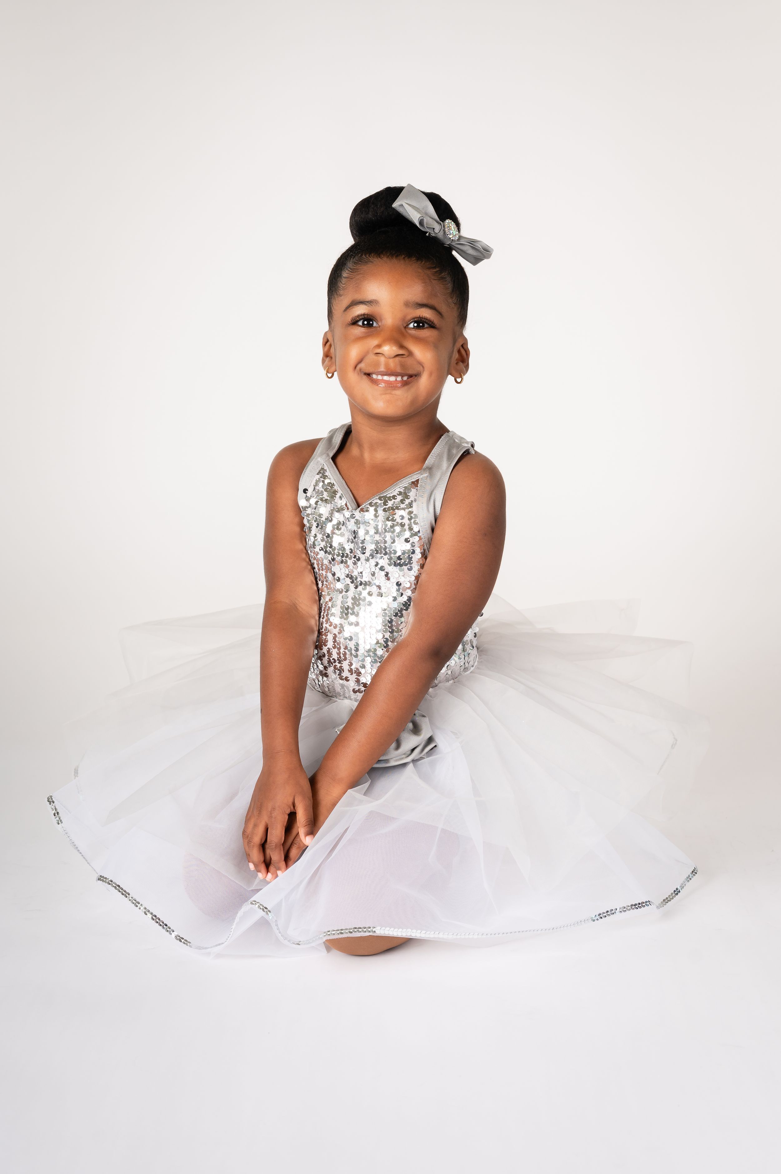 Dancer in silver sequined costume with white tulle skirt performs on white background.