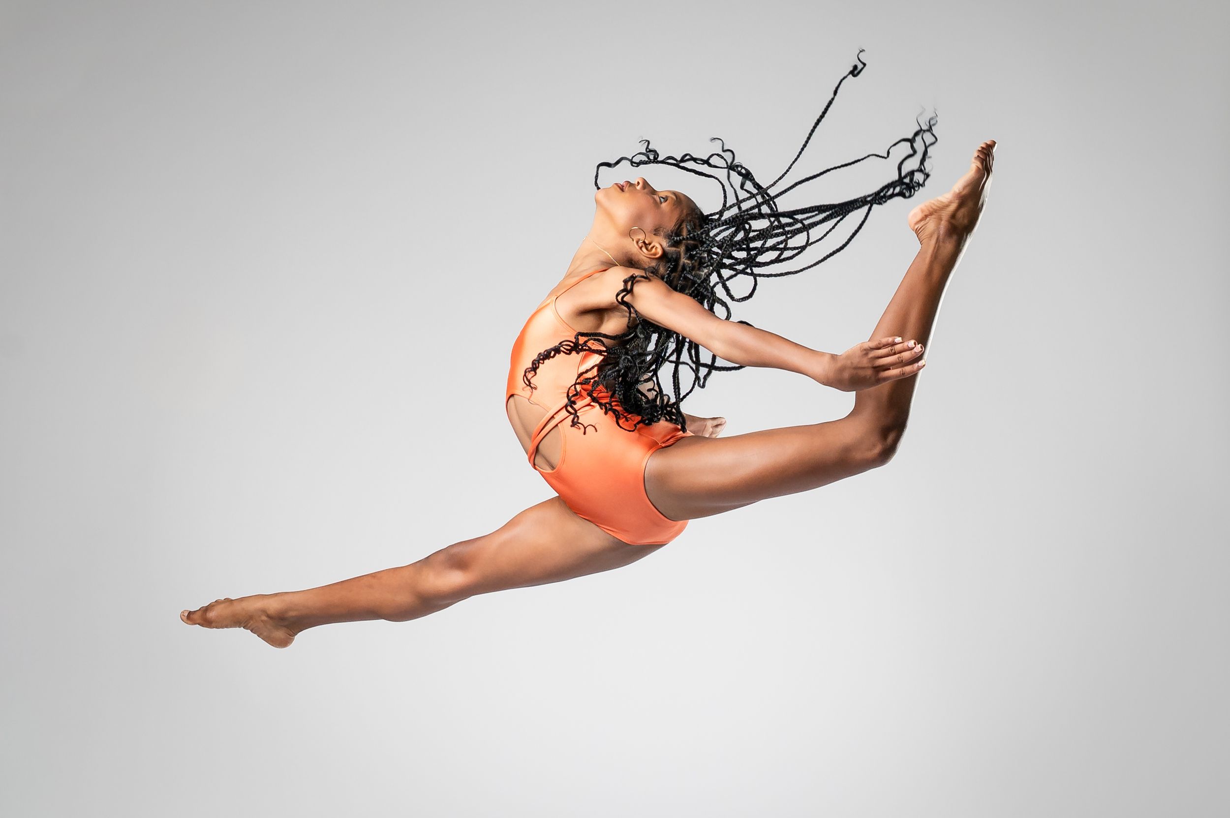 Athletic dancer performs mid-air splits against white studio background.