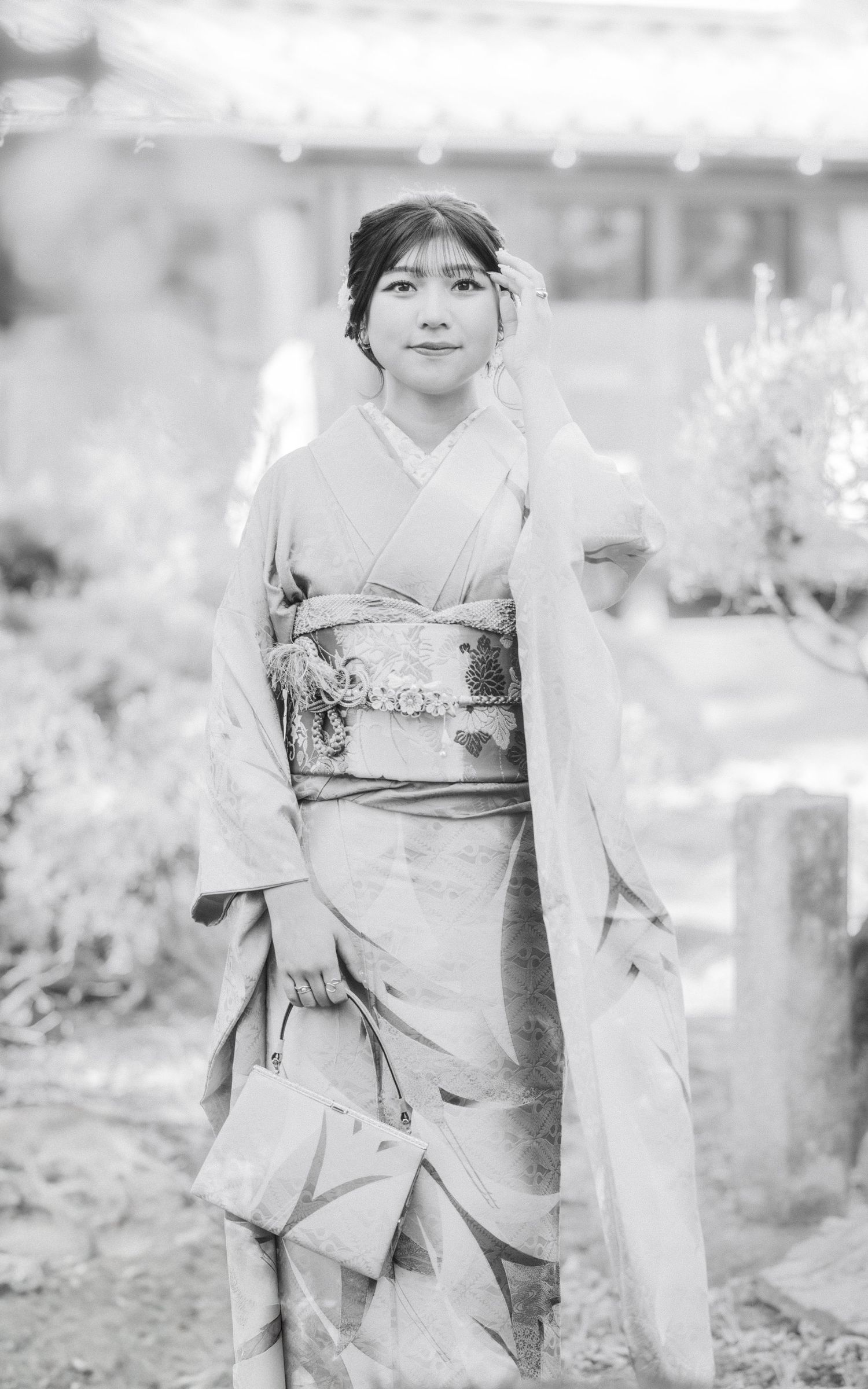 Black and white photo of person in traditional kimono outdoors with garden elements.