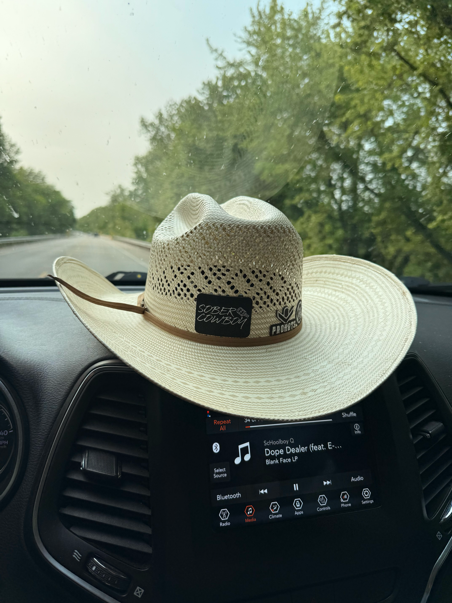 A straw cowboy hat sits on a car dashboard with an infotainment display visible.