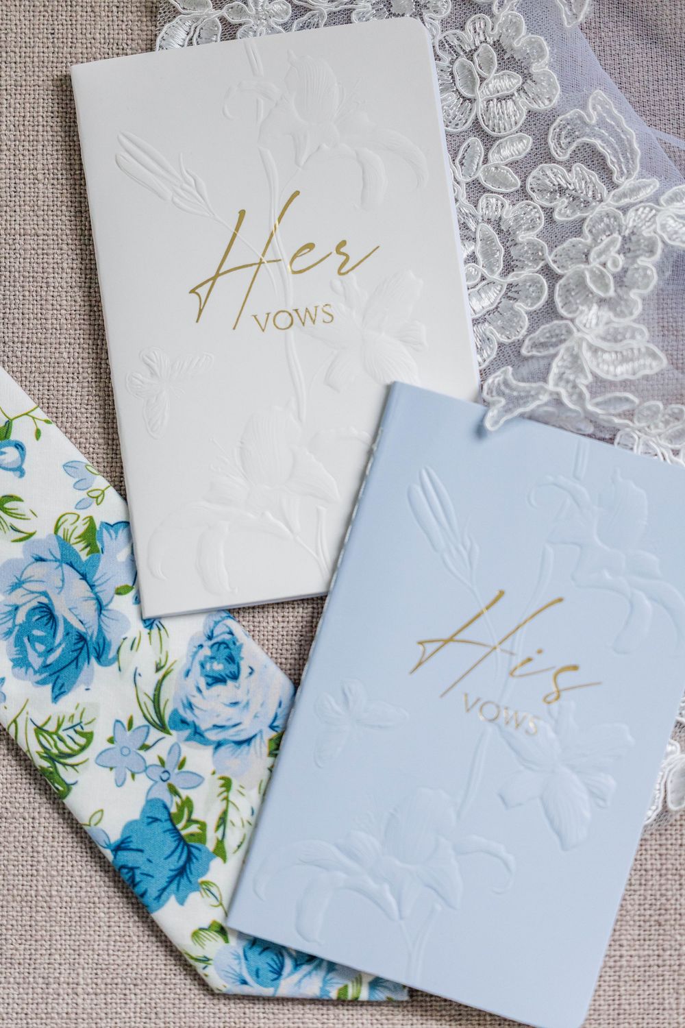 His and Her wedding vow books in white and blue with gold lettering on floral fabric.
