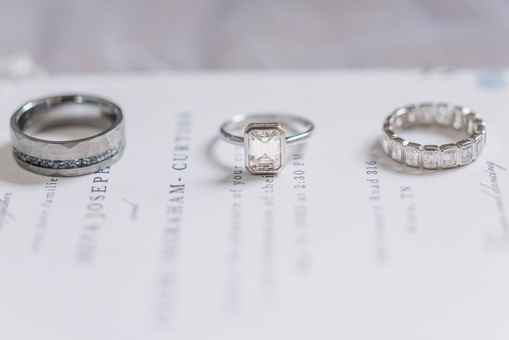 Three wedding rings including an emerald cut engagement ring displayed on invitation paper.