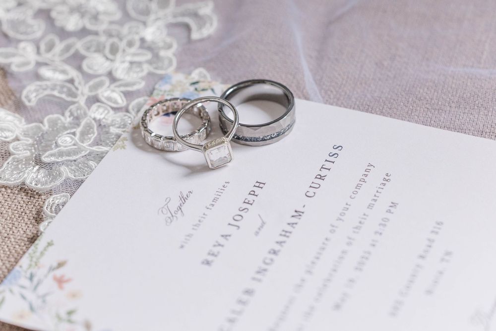 Wedding rings arranged on an elegant floral-detailed wedding invitation with lace accents.
