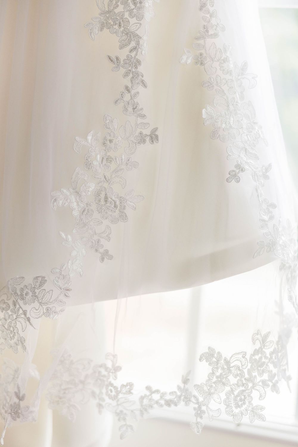 Delicate lace embroidery pattern on sheer white wedding dress fabric in natural light.