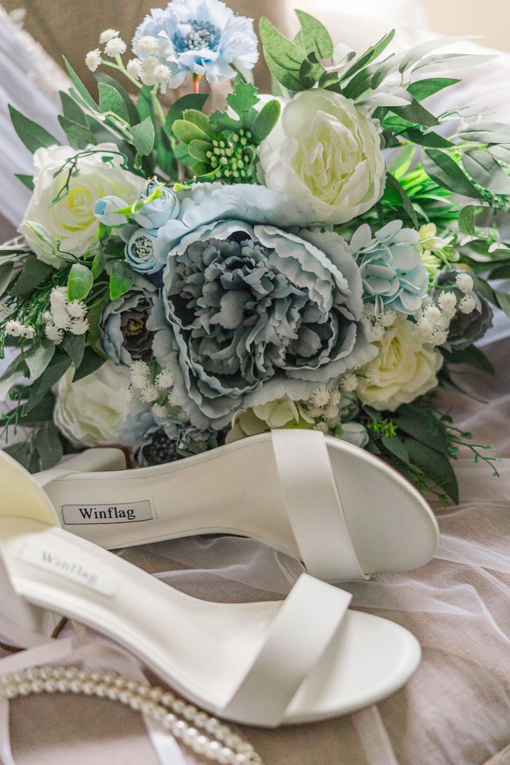 Elegant bridal bouquet of blue and white peonies with white wedding sandals and pearl jewelry.