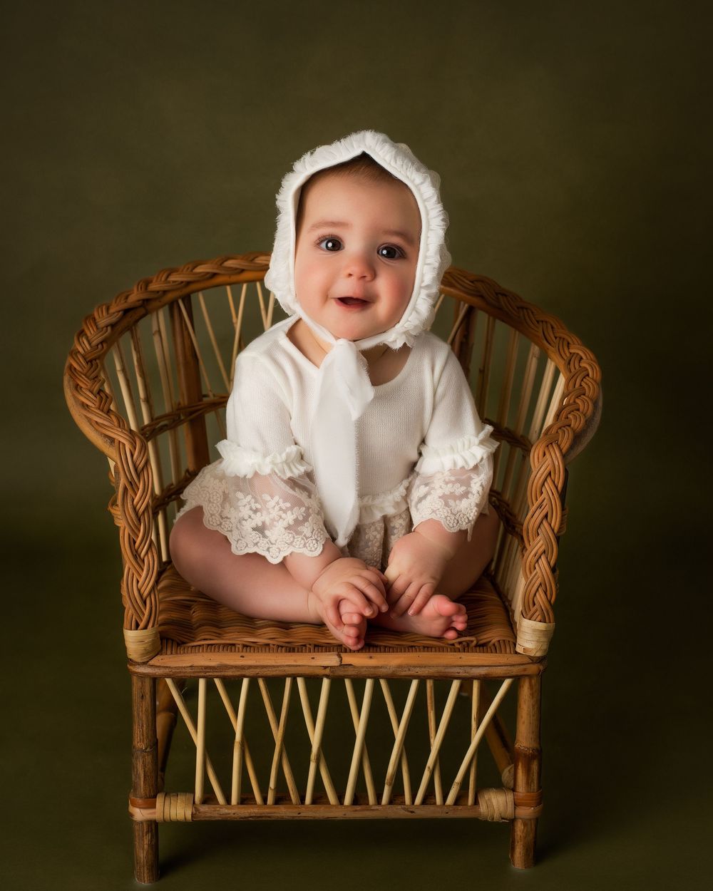 a young child wearing all white sits in a tiny chair against a dark green backdrop during a shoot with a minneapolis photographer