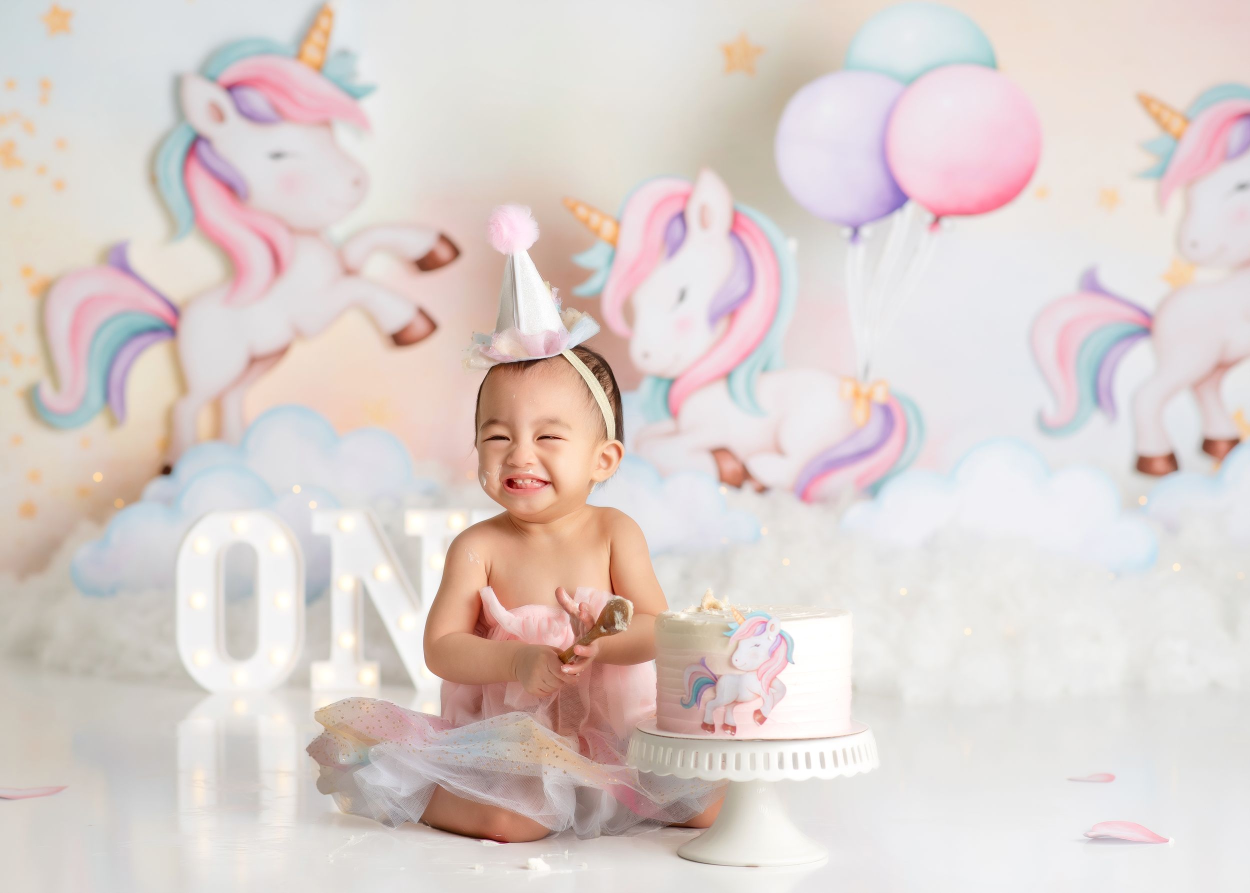 a young girl sits in a unicorn themed studio during her cake smash