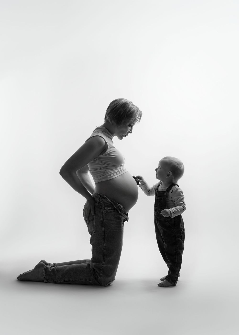 Black and white silhouette portrait of a pregnant person in profile kneeling beside a small child by a minneapolis photographer