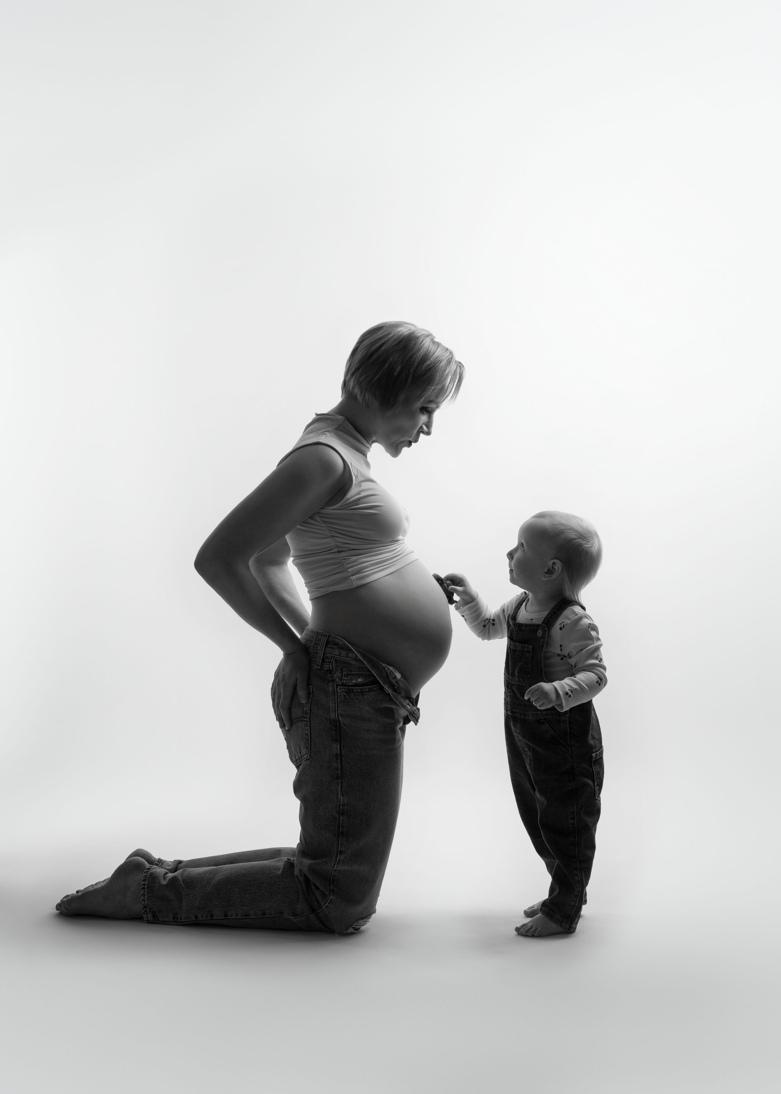Black and white silhouette portrait of a pregnant person in profile kneeling beside a small child by a minneapolis photographer