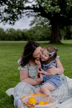 A tender moment shared during a picnic on a grassy lawn under a large tree.