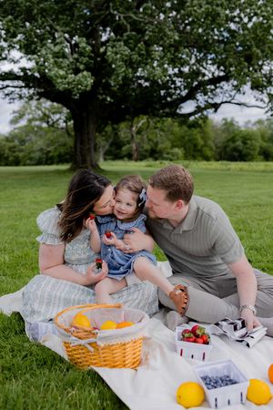 Family sharing intimate moment during picnic with fresh fruit and snacks on blanket.