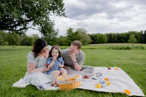 Family having fun together during outdoor picnic on grass under cloudy sky.