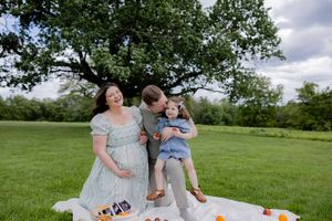 A relaxed family picnic scene in a park with snacks spread out on a blanket under a leafy tree.