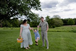 A family enjoying a sunny day outdoors on a green field, with their child playfully walking between them.