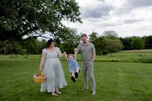 A family enjoying a spring day together on grassy meadow holding hands with a picnic basket.