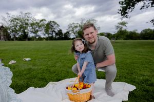 Two people enjoy a spring picnic together on a blanket with a basket of food in a grassy park setting.
