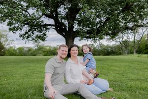 A family sits together on grass under a large tree during a spring outdoor photo session.