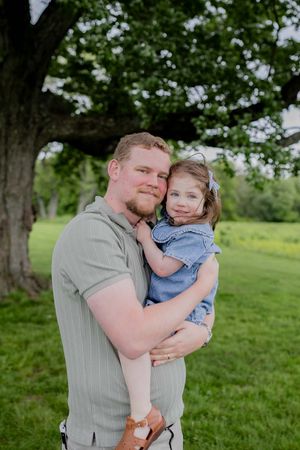 A tender outdoor portrait under a large tree in a lush green park setting.