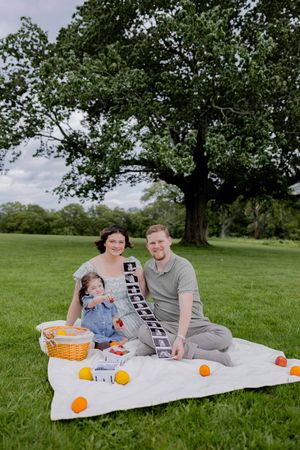 A family having a spring picnic under a large oak tree on a blanket with oranges and a basket.