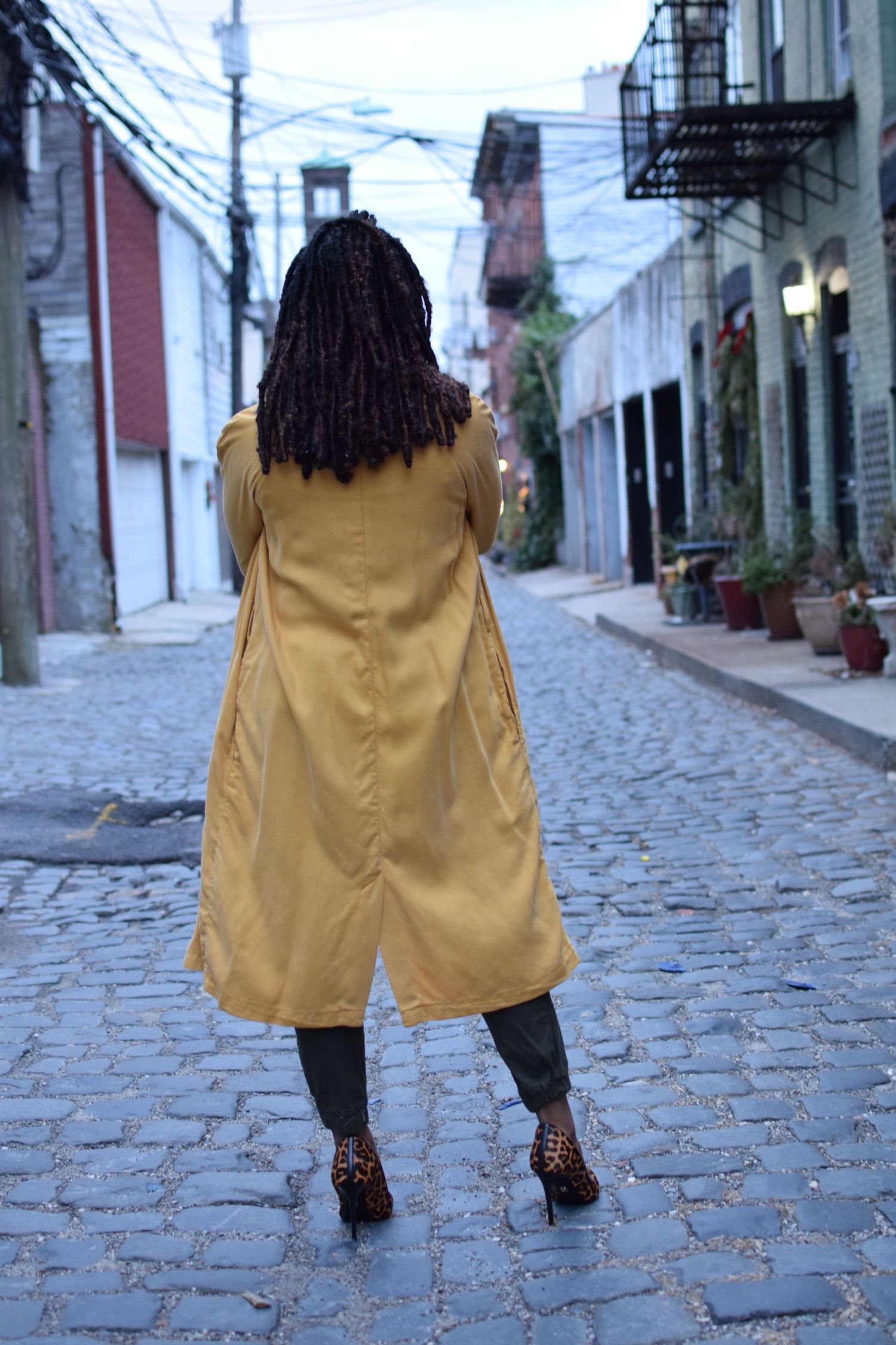 Five sequential shots of someone in a yellow coat walking on historic cobblestone streets.