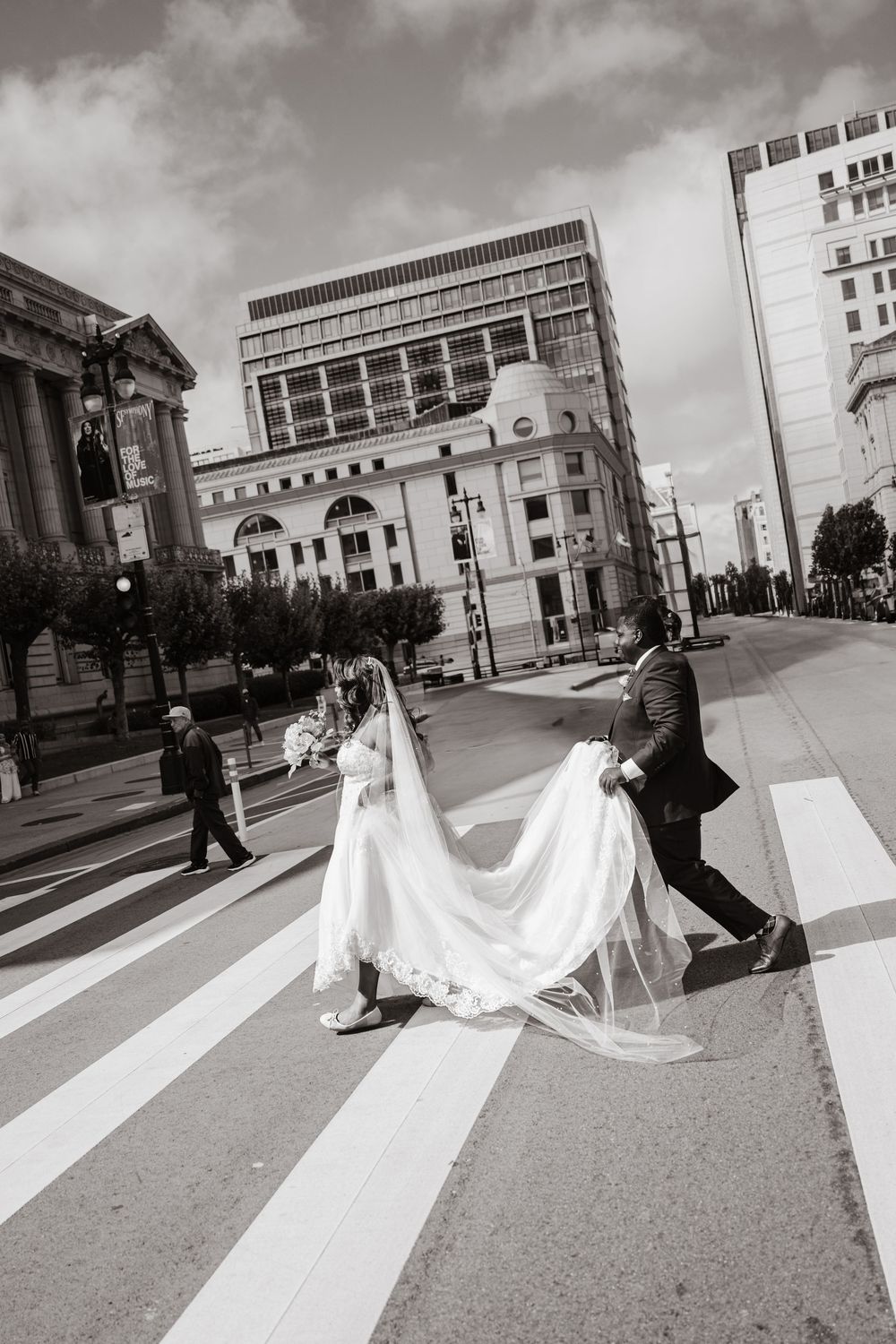 A black and white sequence showing a bride's dress flowing dramatically while crossing a city street crosswalk.