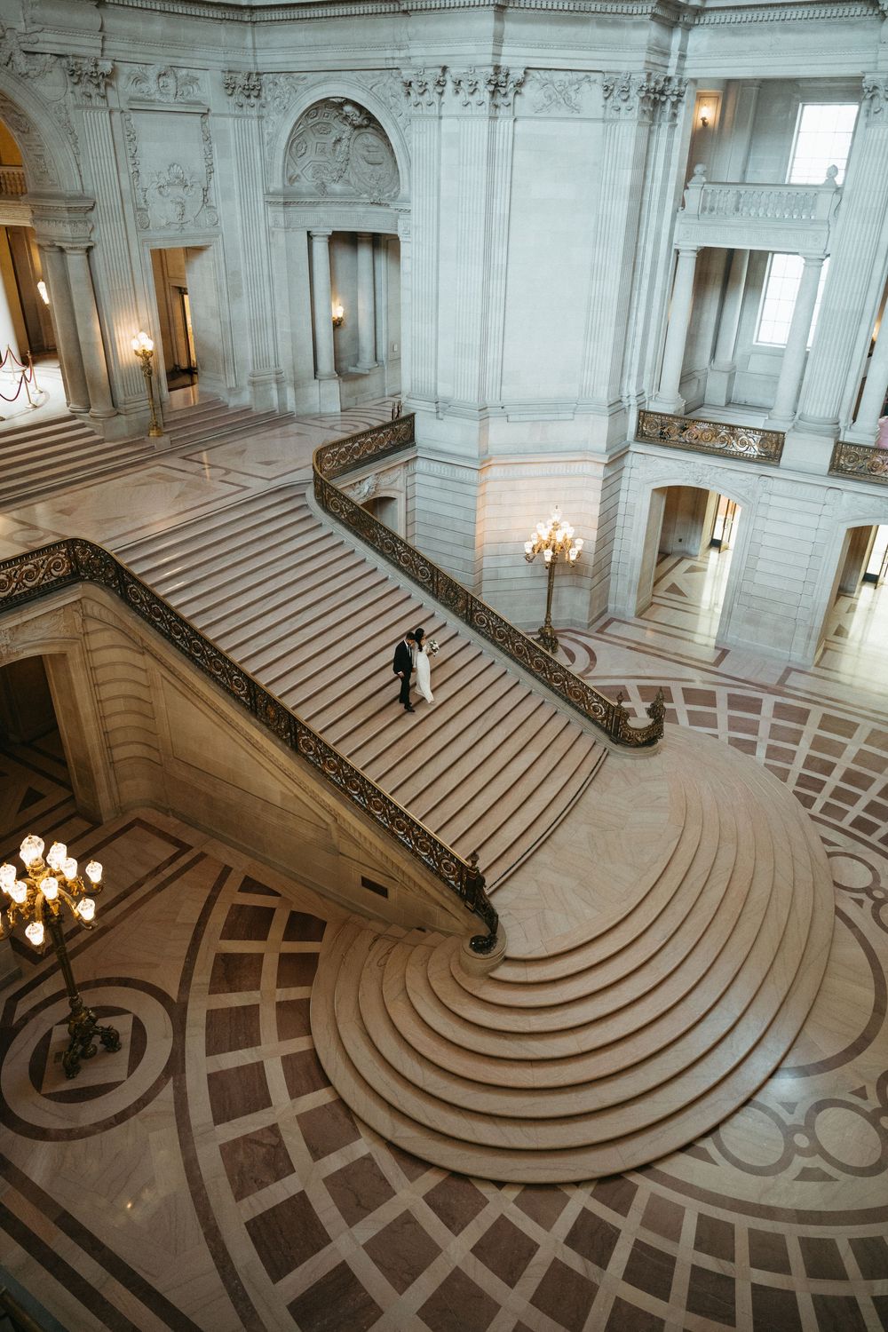 Aerial view of grand marble staircase with curved design and ornate architectural details in San Francisco City Hall.