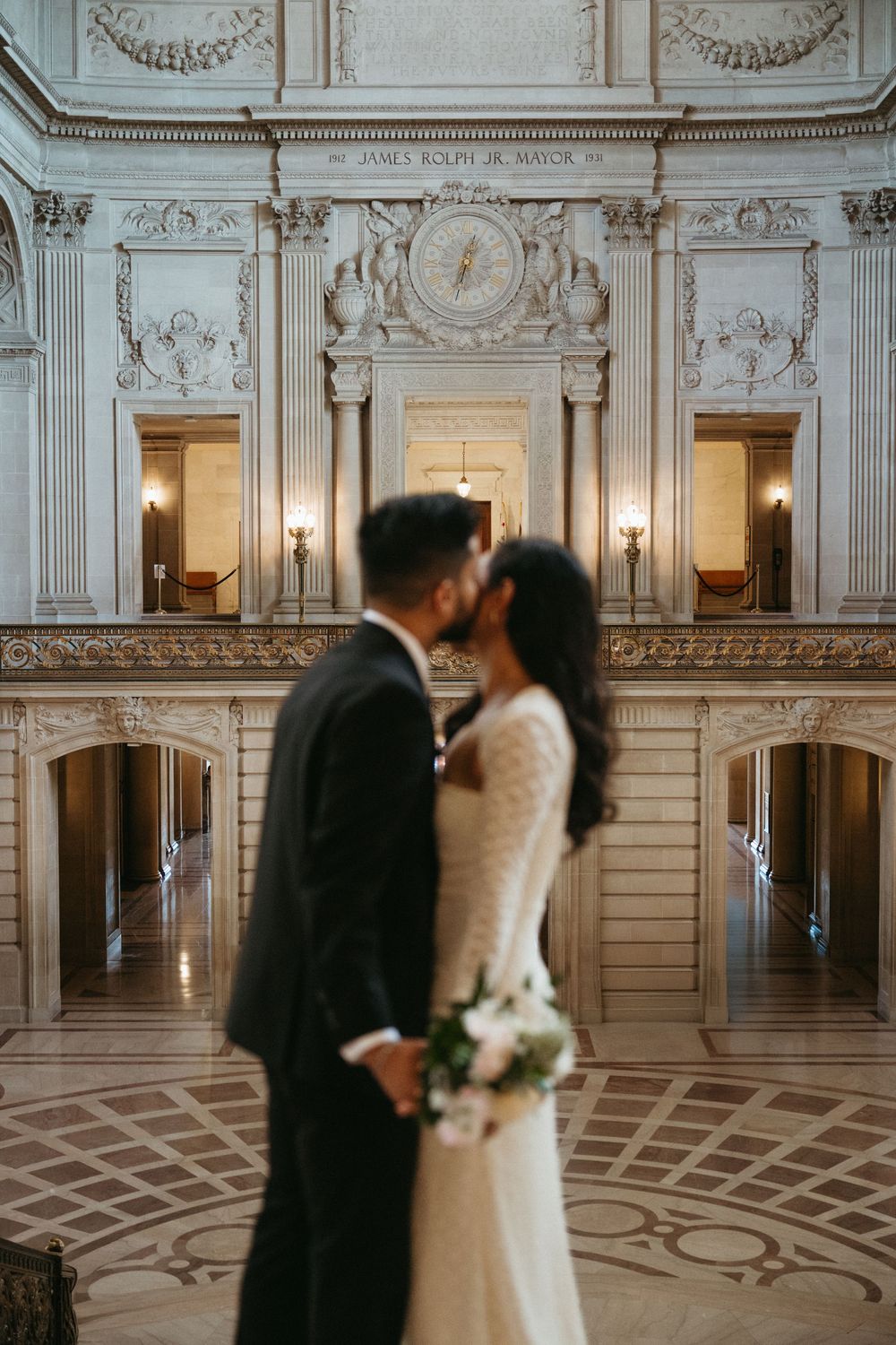 Intimate wedding moment in San Francisco City Hall's grand marble interior with ornate Beaux-Arts architecture and warm lighting.