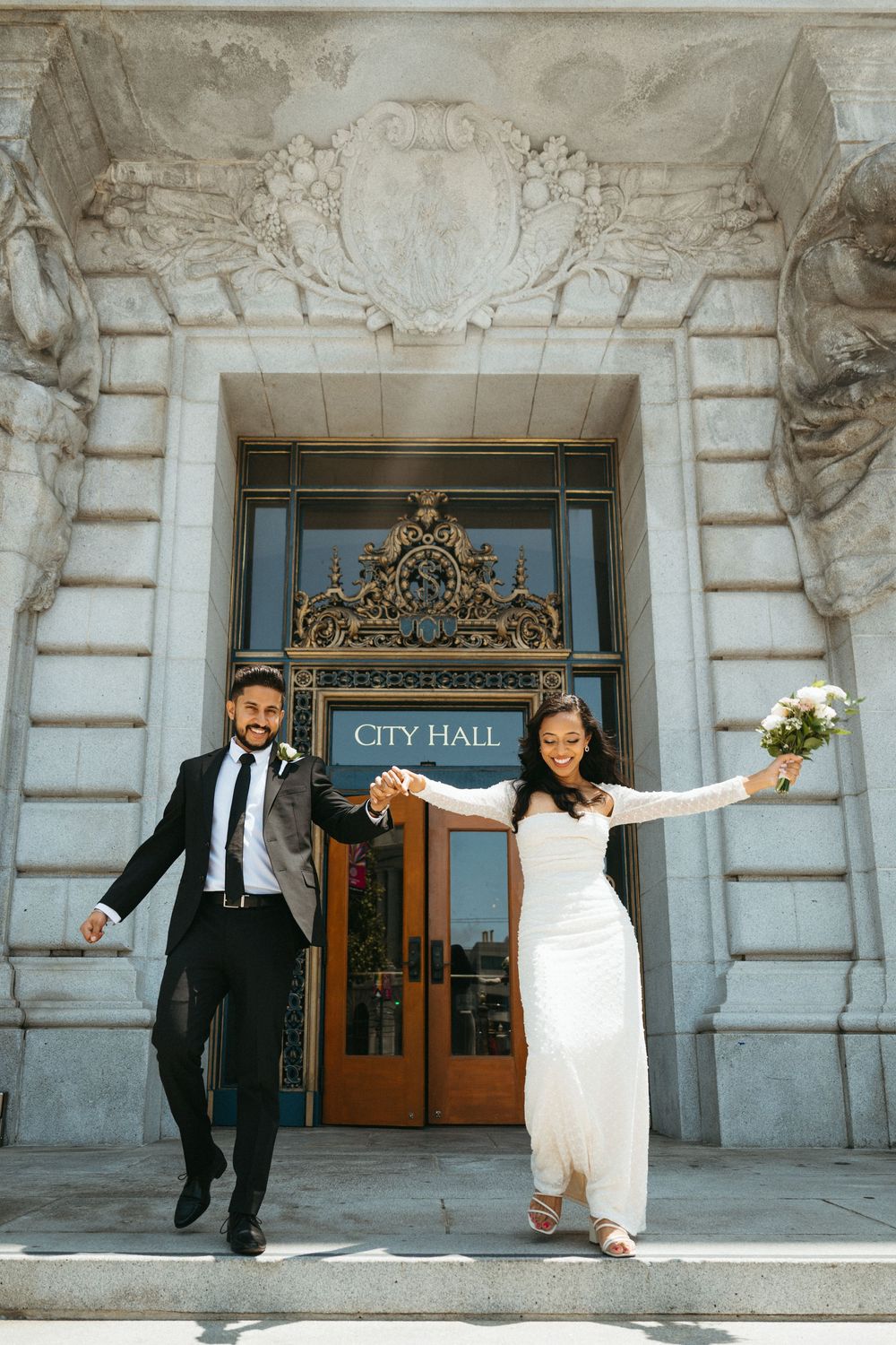 A joyful couple celebrating outside historic City Hall with its ornate stone facade and decorative entrance.