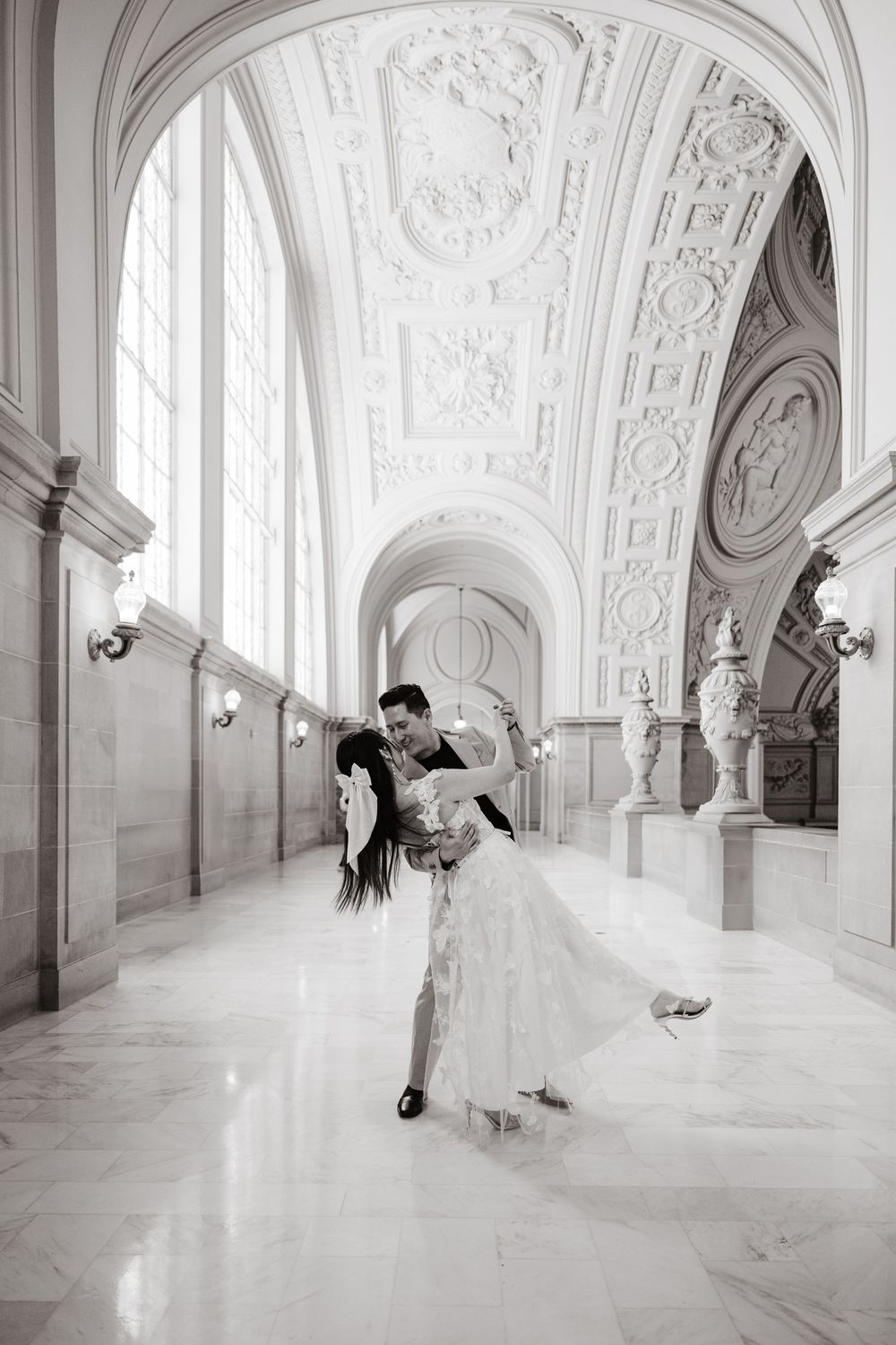 A romantic wedding couple dances gracefully in an ornate white marble corridor with elegant architectural details.