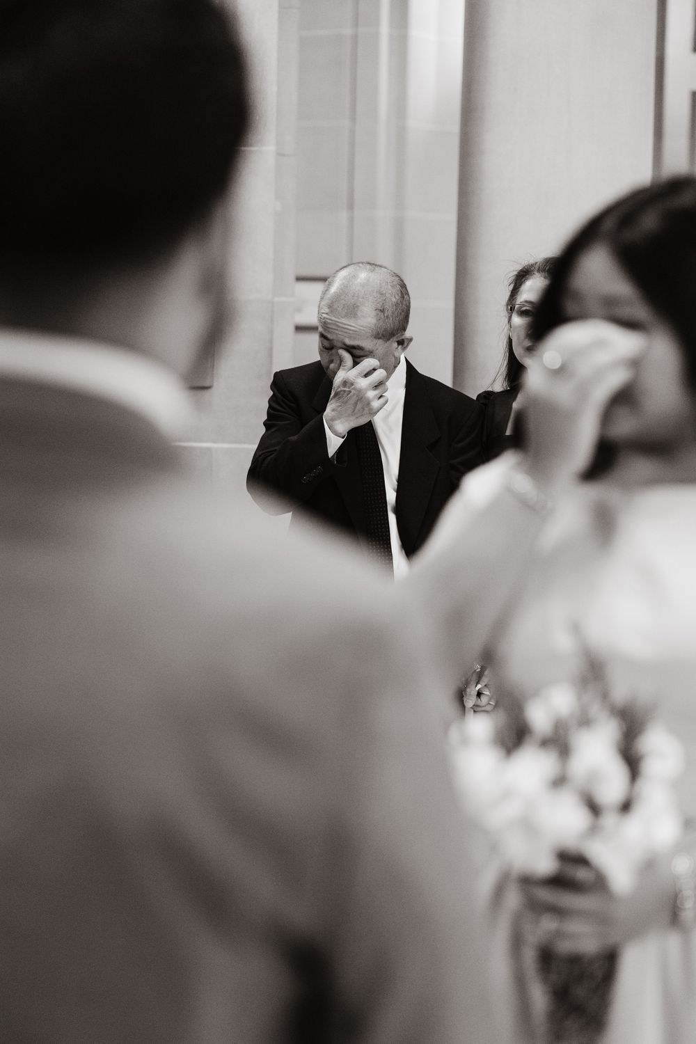 Emotional father wiping tears at wedding ceremony in black and white photography.