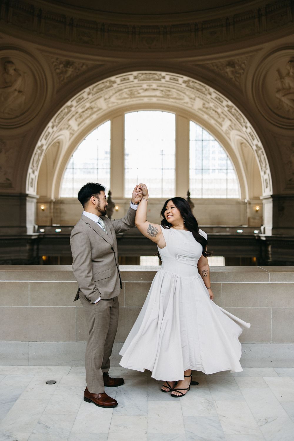 Couple dancing in elegant wedding attire inside San Francisco City Hall's grand rotunda with ornate arched architecture.