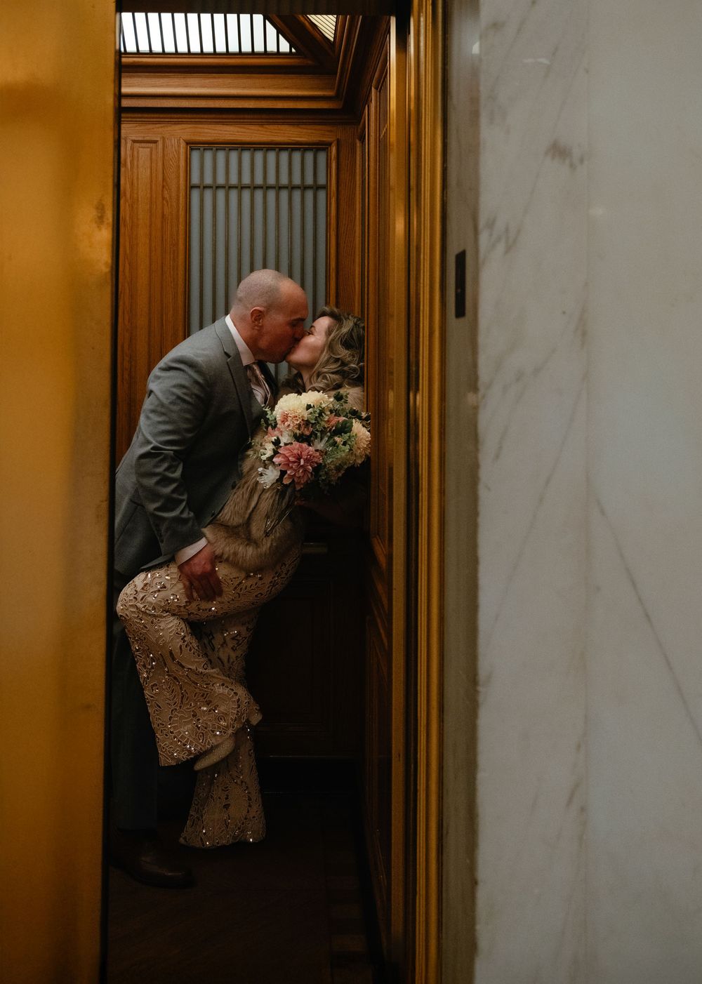 Two people embracing in an elevator, with one holding a colorful bouquet of flowers.