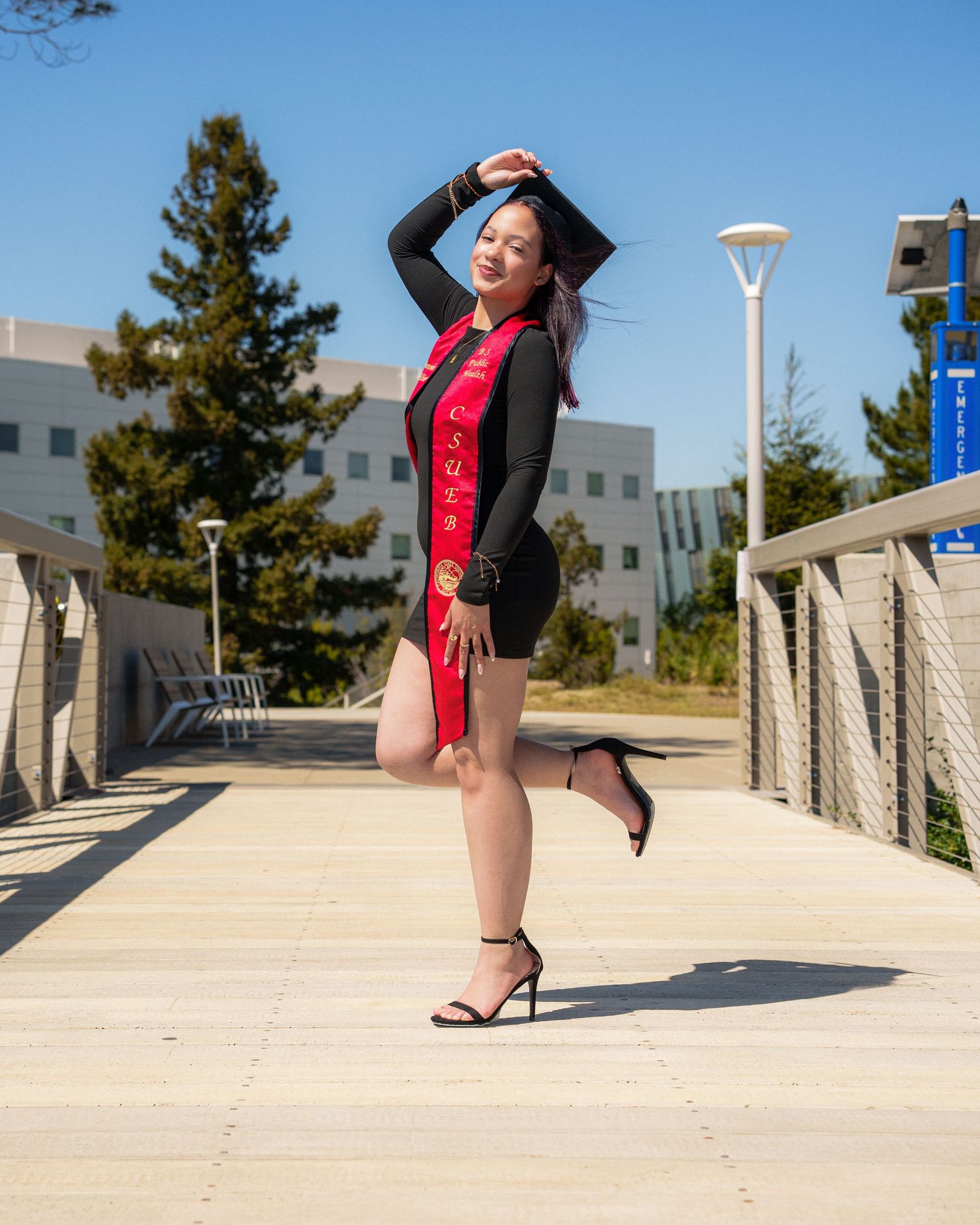 Graduation portraits photography. figure in a red and black outfit strikes dramatic poses on a concrete path against a sunny urban backdrop.